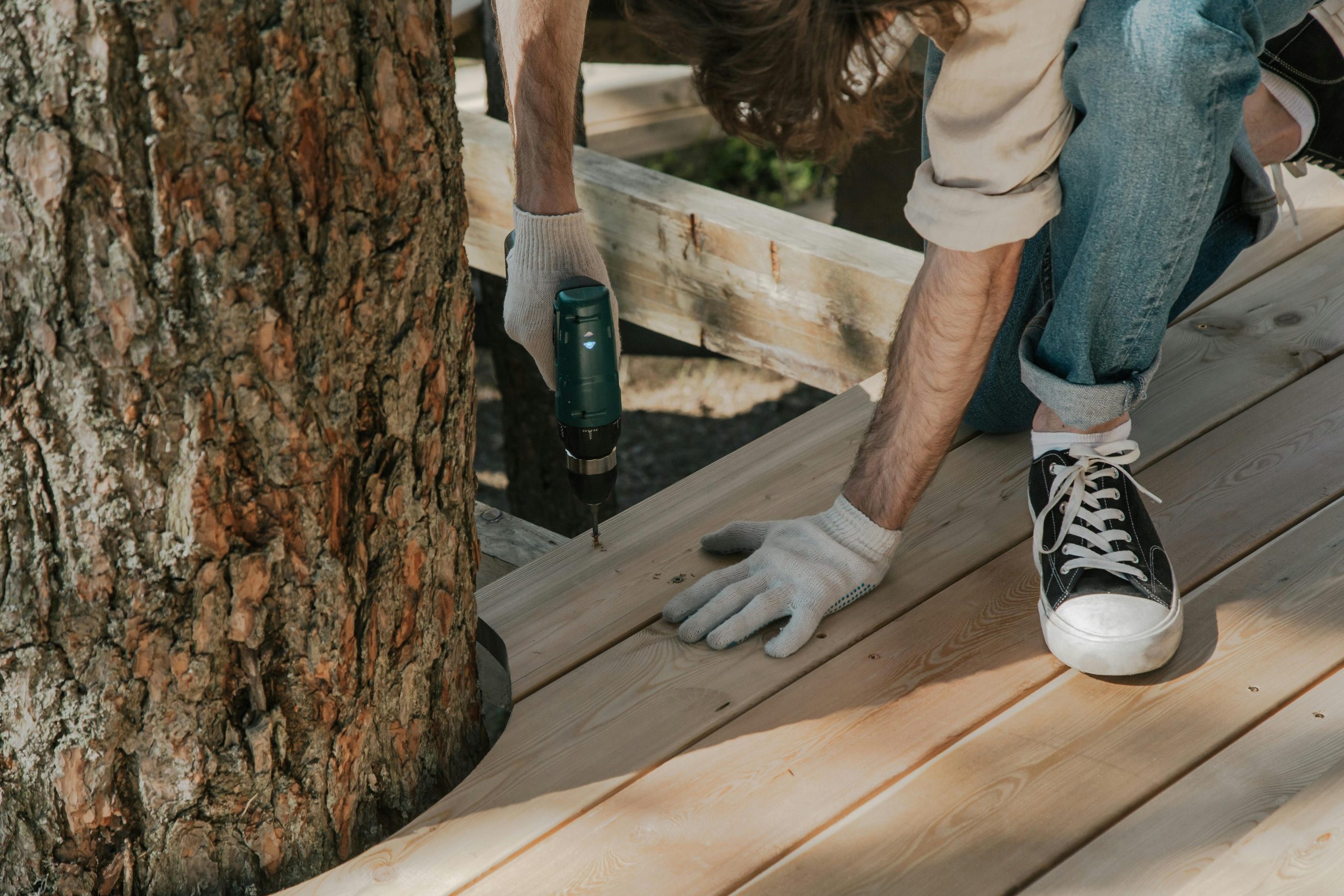 man drilling wooden planks on a deck